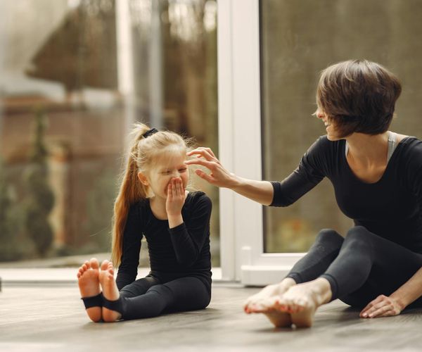 Children laughing while trying to do a partner yoga pose.