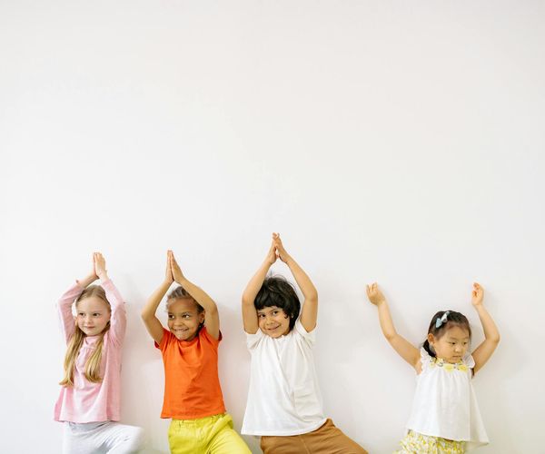Group of kids playfully imitating animal yoga poses in a bright room.